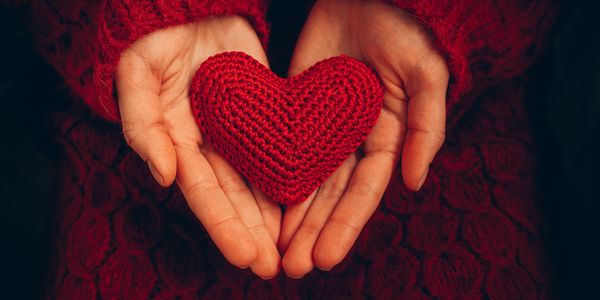 Hands holding a red knitted heart.