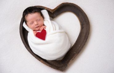 baby with dark hair, sleeping in a heart, holding a red heart
