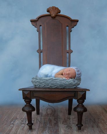 newborn baby sleeping on blue pillow on tall chair