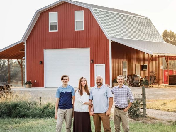 Family of four standing in front of a red barn.