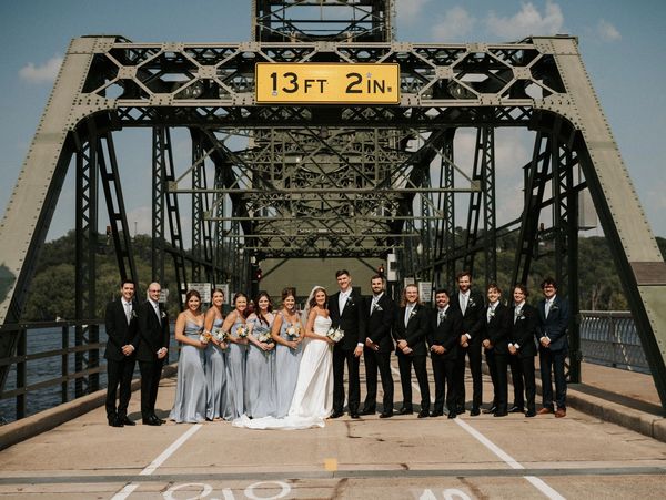 Wedding party posing on a steel bridge under a clearance sign.