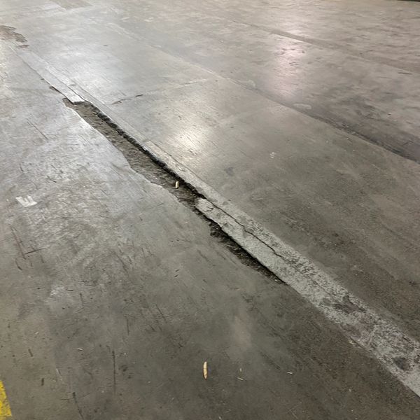 Cracked concrete floor with a long, narrow fissure in an indoor setting.