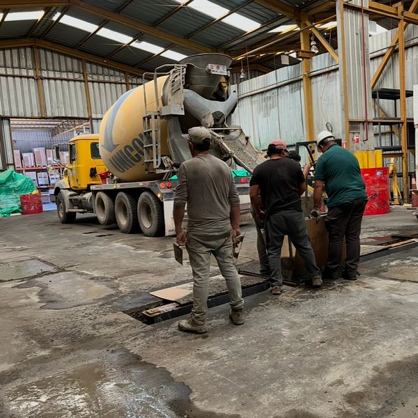 Three workers operating a concrete mixer truck inside an industrial warehouse.