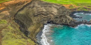 A coastal cliff with green grass and turquoise ocean waves crashing on the shore.