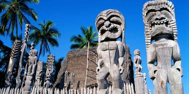 Traditional wooden tiki statues with palm trees under a clear blue sky.