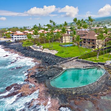 Coastal resort with a natural lava rock pool and palm trees under a blue sky.