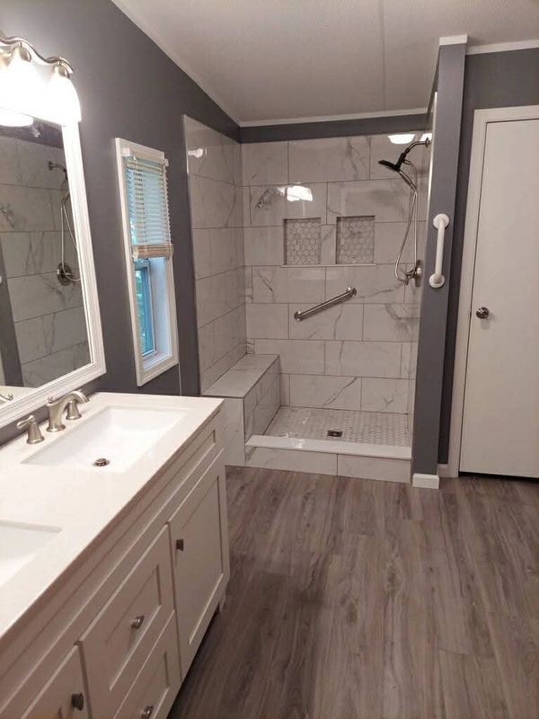 Modern bathroom with white vanity, gray walls, and tiled walk-in shower with bench.