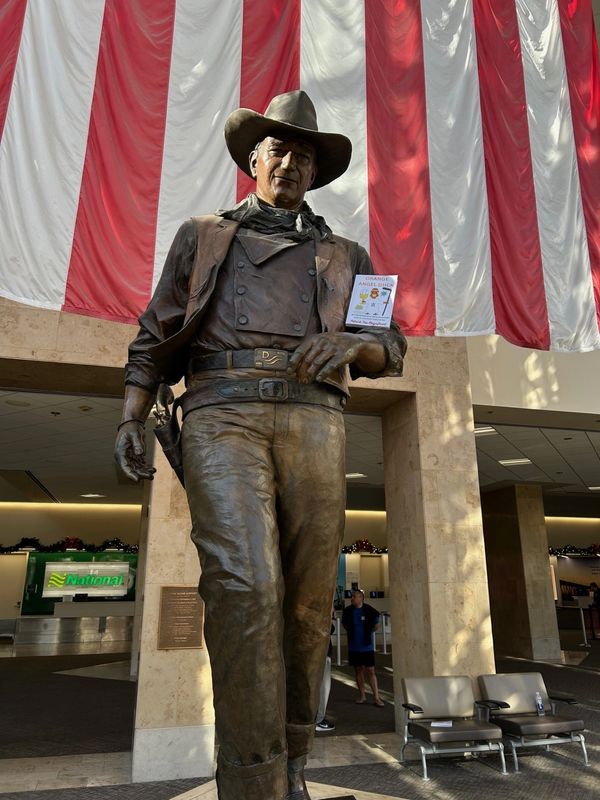 John Wayne statue at Orange County Airport seen with Orange Angel Duck Book.
