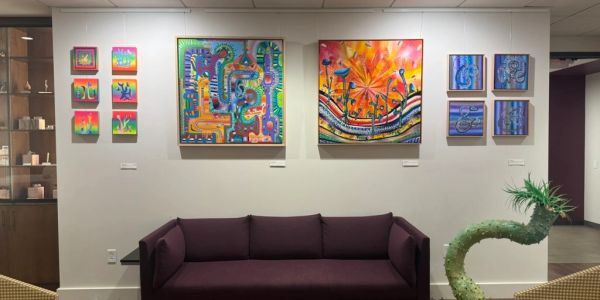 Colorful abstract paintings displayed on a white wall above a dark purple couch.