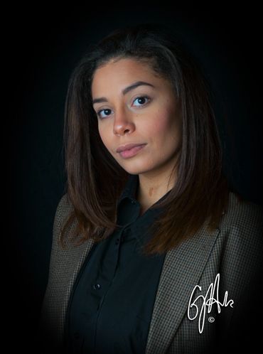 Confident young woman in a blazer against a dark background.