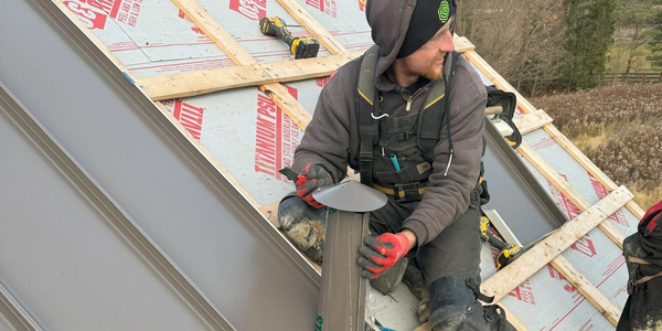 Worker installing metal roofing on a sloped roof under cloudy skies.