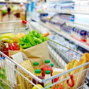 Shopping cart filled with fresh groceries in a supermarket aisle.