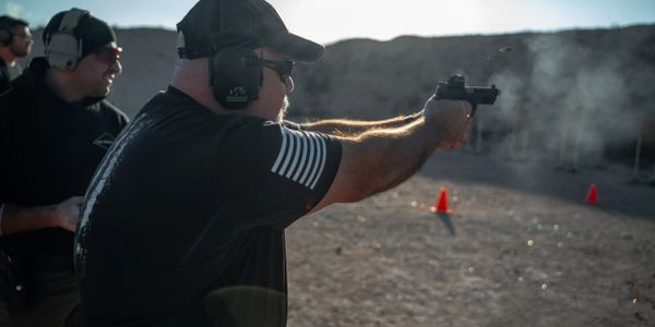 Man wearing ear protection firing a handgun outdoors in black and white.