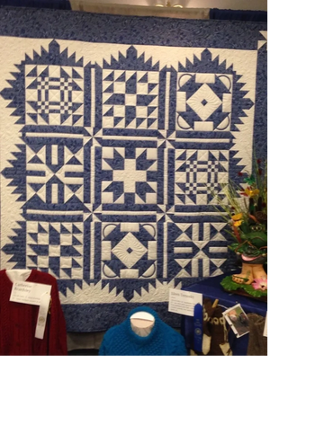 Blue and white patchwork quilt with geometric patterns displayed at a craft show.