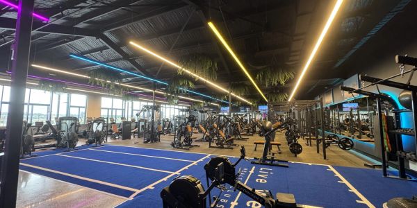 Modern gym with workout machines and blue exercise mats under bright lights.