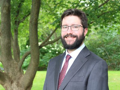 Man in suit and glasses smiling outdoors.