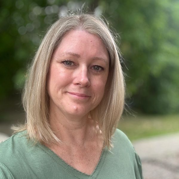 A woman with blonde hair smiling gently outdoors.