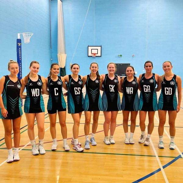 Women's netball team posing on court in uniforms.
