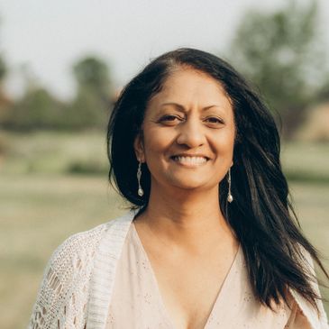 A smiling woman in a light pink dress and white cardigan outdoors.