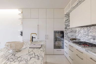 Modern kitchen with white cabinets and marble countertops.