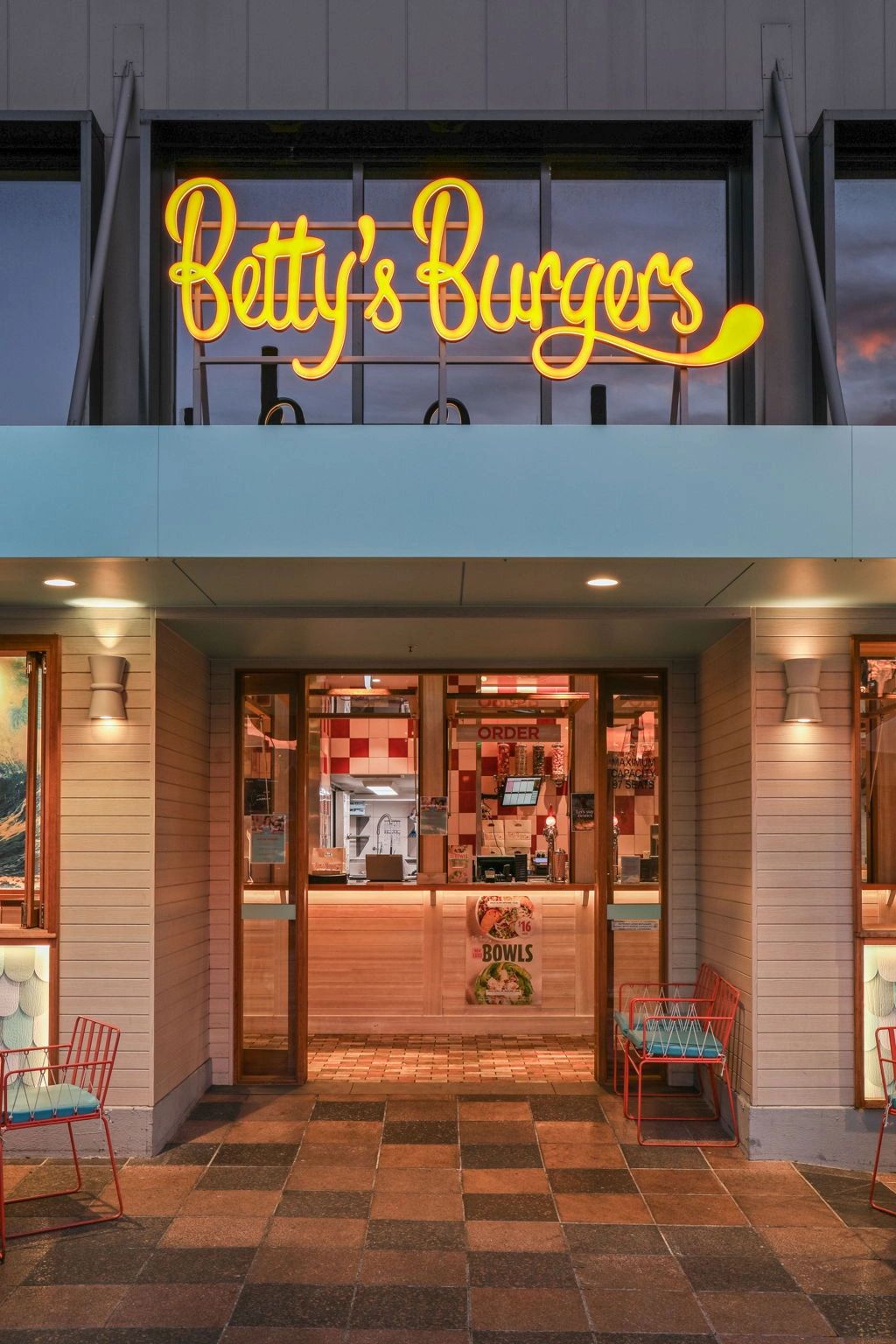Entrance of Betty's Burgers with bright neon sign and outdoor seating.