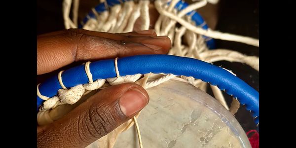 Hand weaving white cords around a blue ring, close-up.
