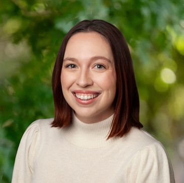 Smiling woman with shoulder-length brown hair in a white turtleneck sweater.