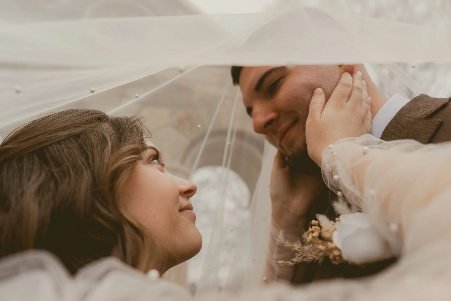 Bride and groom tenderly gaze at each other under a veil on their wedding day.