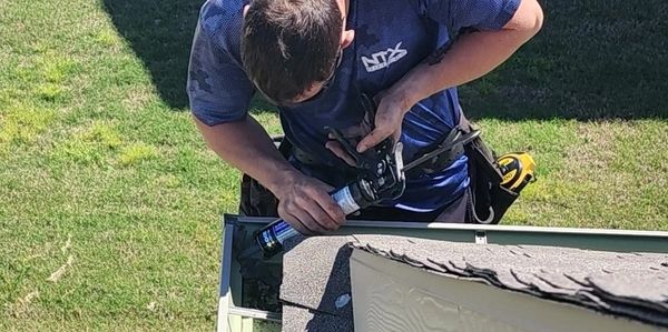 North Texas Gutters employee working on a gutter repair with a glue gun on a ladder