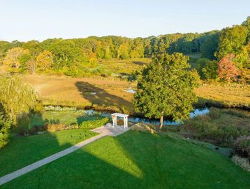 A serene landscape with green grass, a small pavilion, and a pond surrounded by trees.
