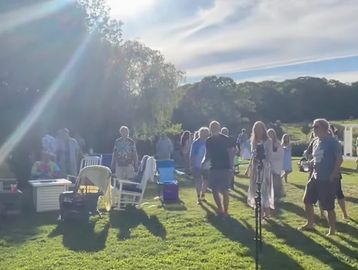 People gathering outdoors on a sunny day with chairs and coolers.