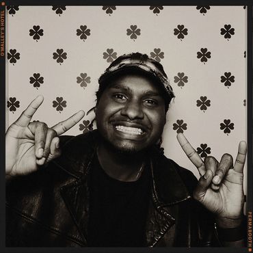 Man in leather jacket making a hand gesture and smiling.