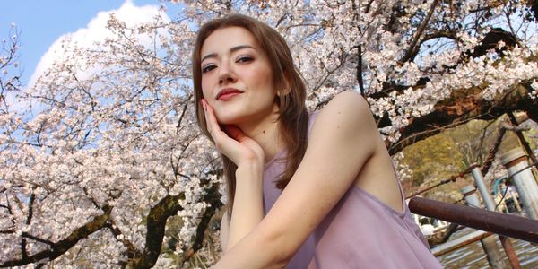 Young woman posing under blooming cherry blossoms on a sunny day.