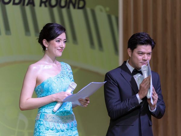Two presenters in formal attire holding microphones and papers on stage.