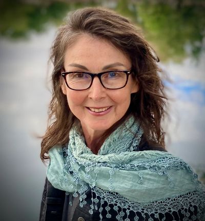 Smiling woman with glasses and a light blue scarf outdoors.