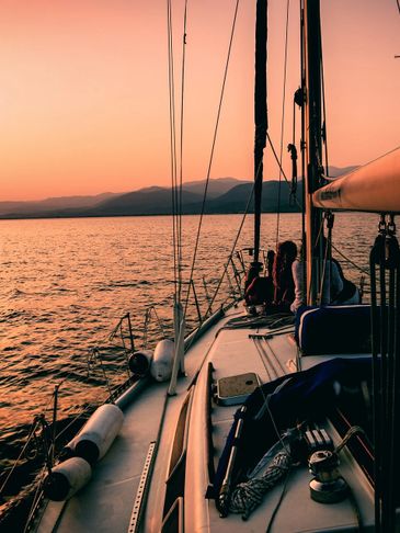 Sailboat cruising at sunset with calm waters and distant mountains.