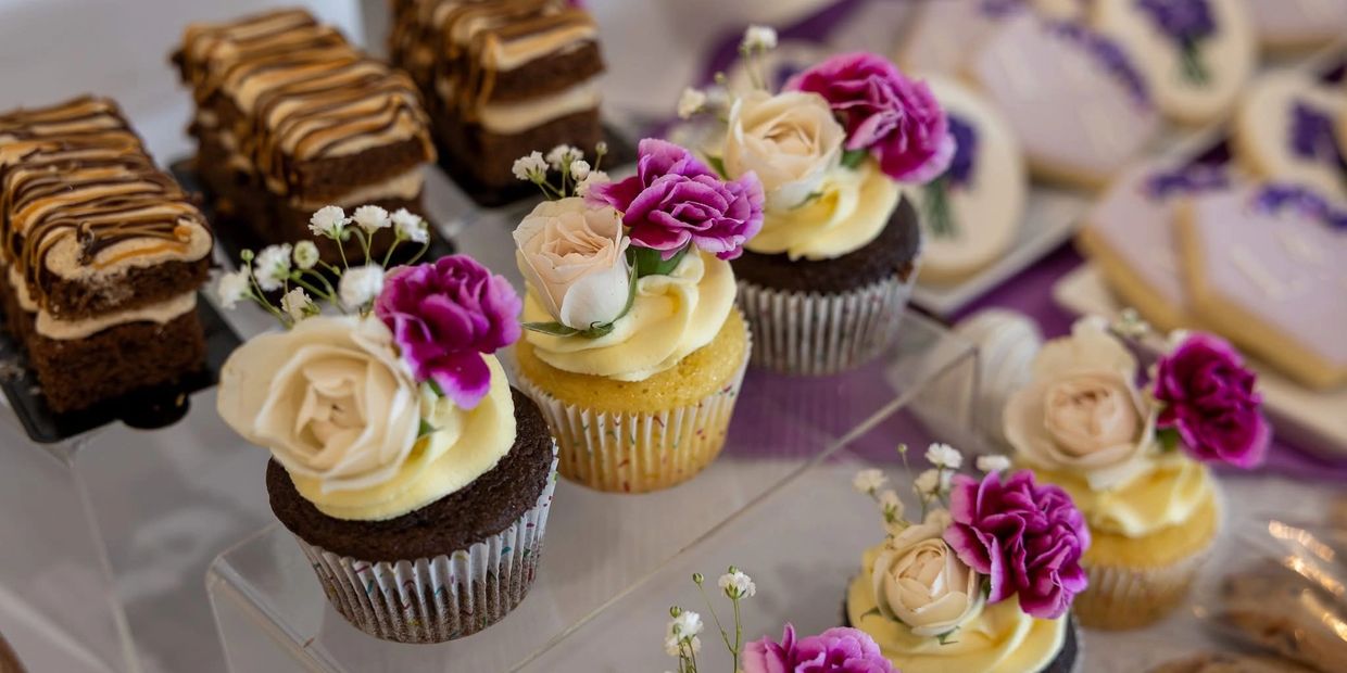 Cupcakes decorated with cream and fresh flowers among assorted desserts.