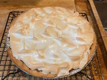 A freshly baked pie topped with golden brown meringue cooling on a rack.