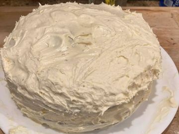 A homemade cake with thick white frosting on a plate.