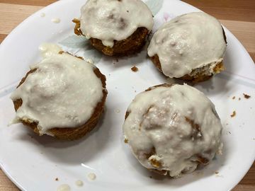Four cinnamon rolls with white icing on a white plate.