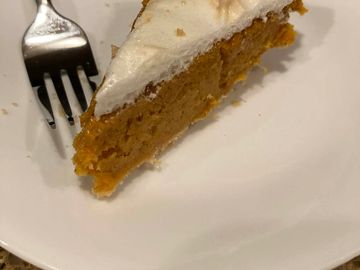 A slice of pumpkin pie with whipped cream on a white plate.