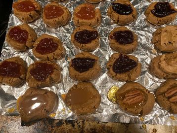 Peanut butter cookies topped with various jams and pecans on foil.