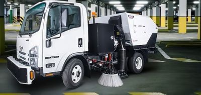 Compact street sweeper truck cleaning an indoor parking lot.