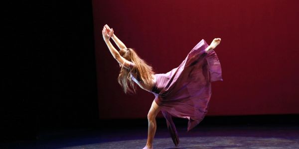A dancer in a flowing purple dress performs on stage against a dark red backdrop.