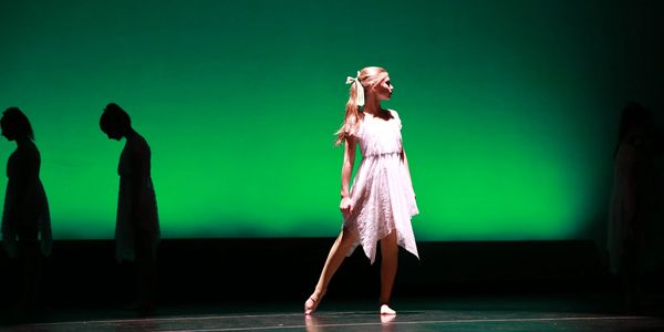 A girl in a light dress dances under green stage lighting.