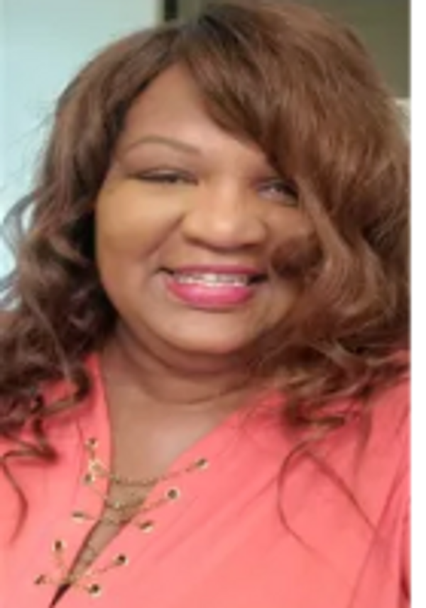 Smiling woman with wavy brown hair wearing a coral top.