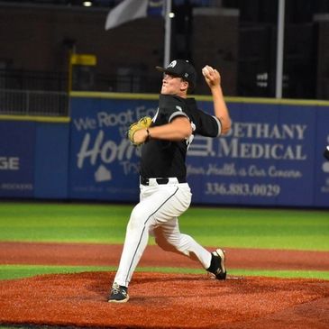 Baseball pitcher in mid-throw on the mound during a night game.