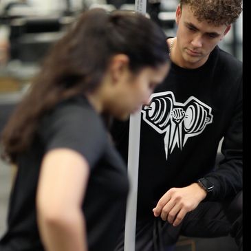A trainer watches a woman stretching her leg in a gym.