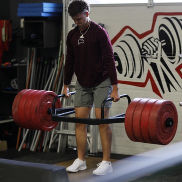 Young man lifting heavy weights with a trap bar in a gym.