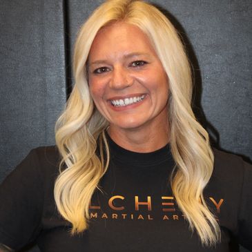 Smiling woman with long blonde hair wearing a black martial arts shirt.